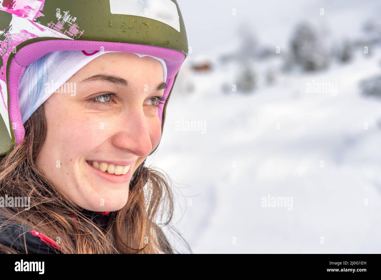 Woman with brown hair, wearing a ski helmet smiling while looking to the right side of the