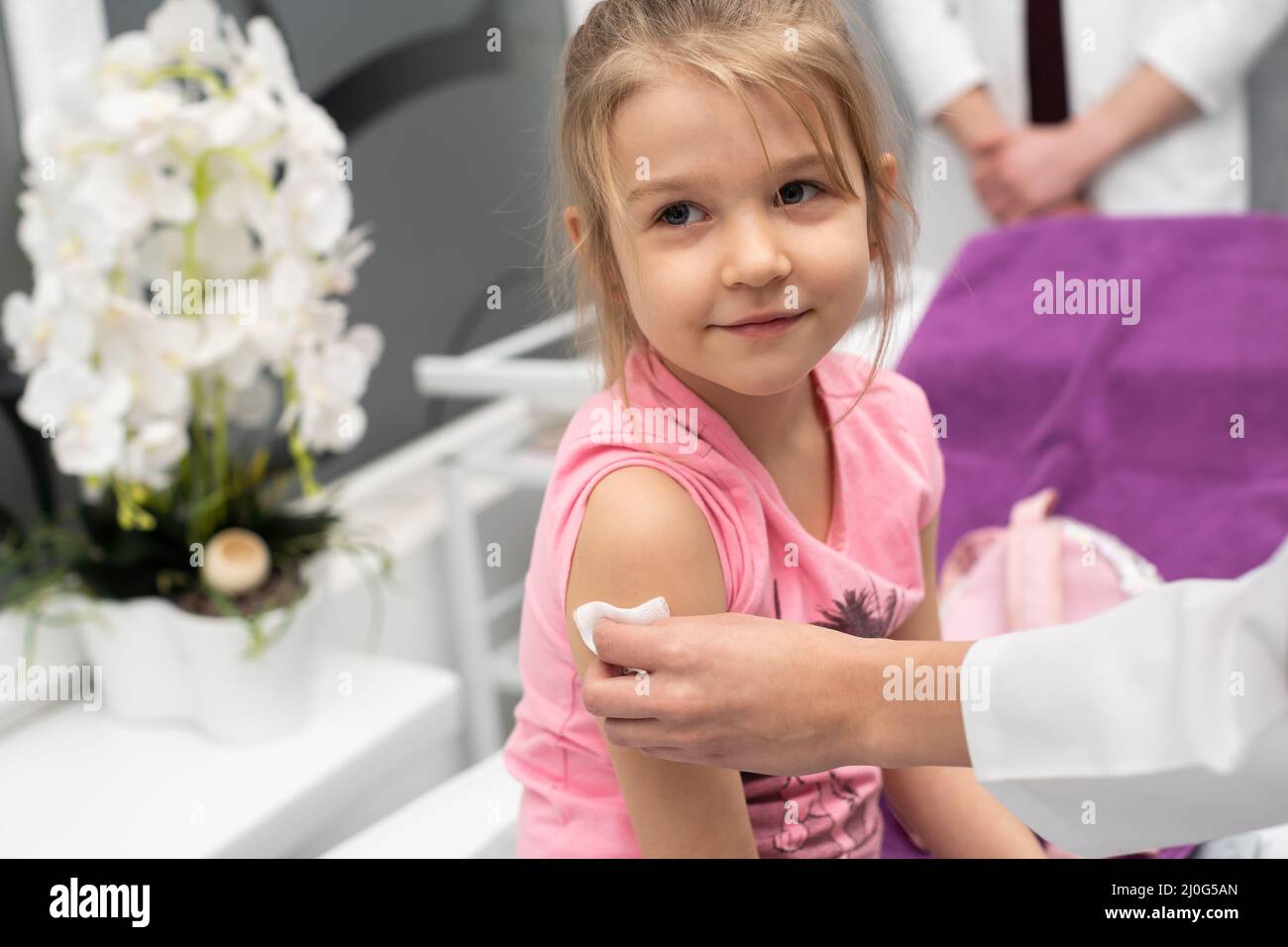 The girl is looking outside the frame. A young lady doctor is preparing a child for an injection by disinfecting a piece of skin Stock Photo