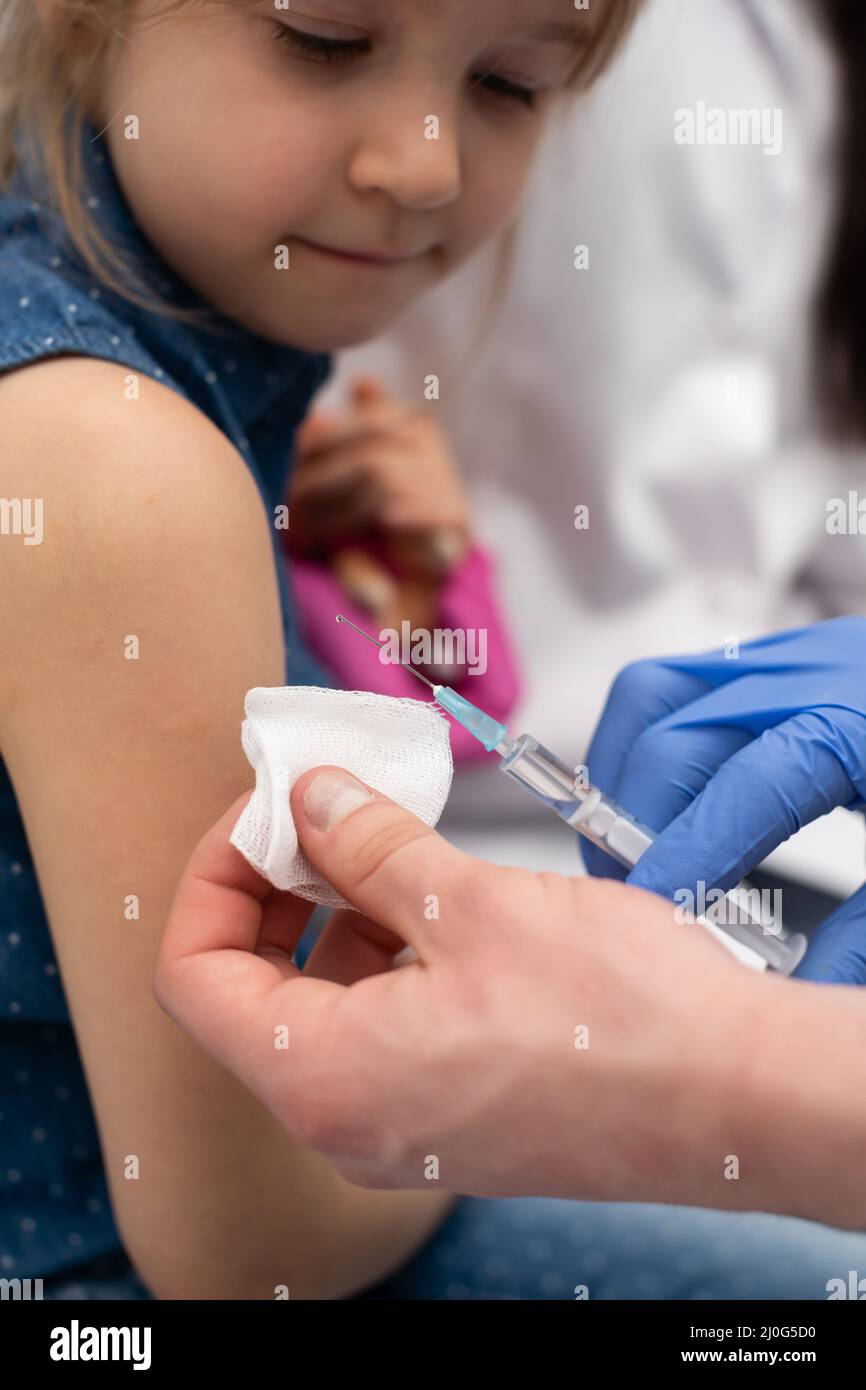 The doctor is getting ready to vaccinate a little girl. A young nurse sits next to the child to make the child feel safe. Preven Stock Photo