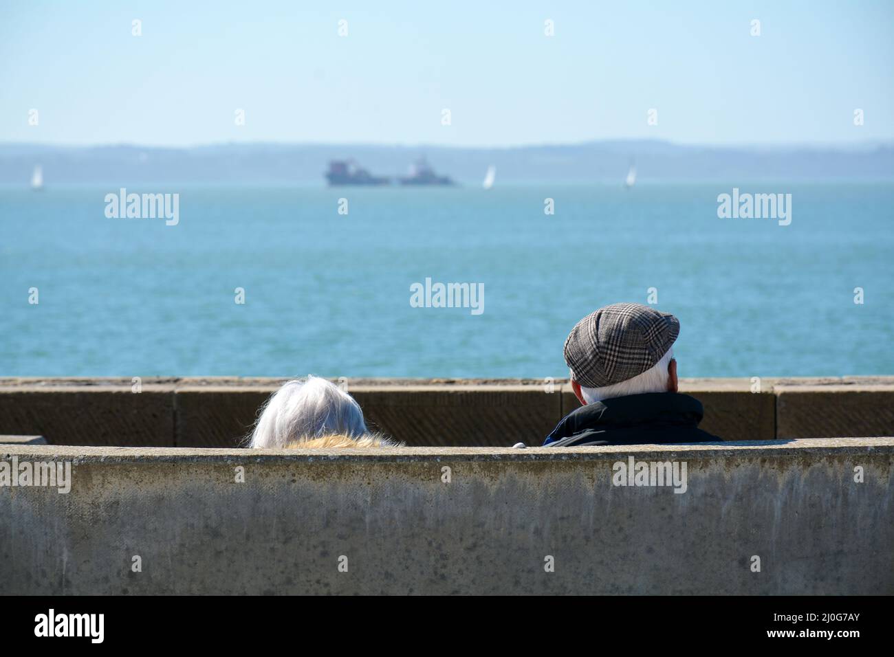 Elderly couple sit on a bench by the coast watching out to sea Stock ...