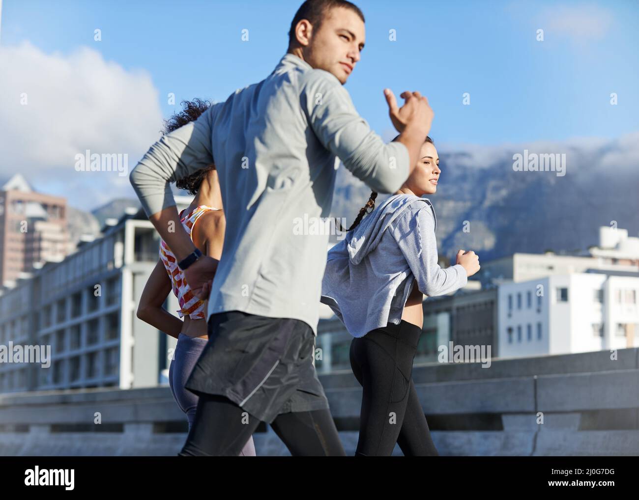 We push each other further. Shot of a group of friends jogging together through the city. Stock Photo