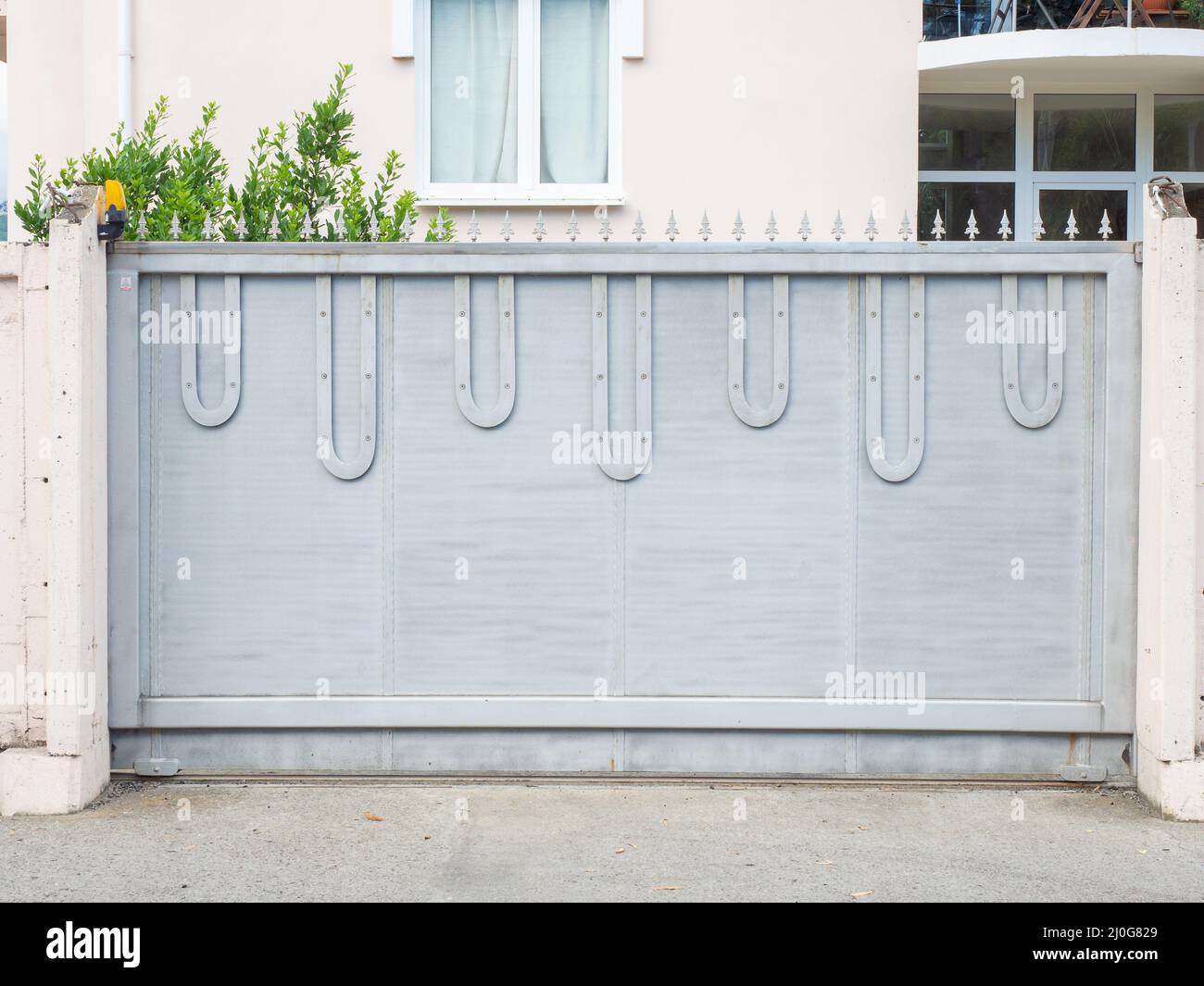 Blue-gray iron gates with sharp points on top are located in front of a lightcolored residential building Stock Photo