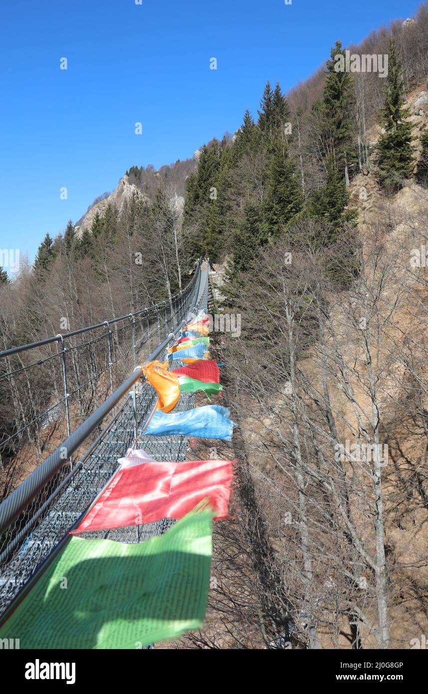 many colorful Tibetan flags symbol of peace and prayer weighs a suspension bridge between the mountain ridges Stock Photo