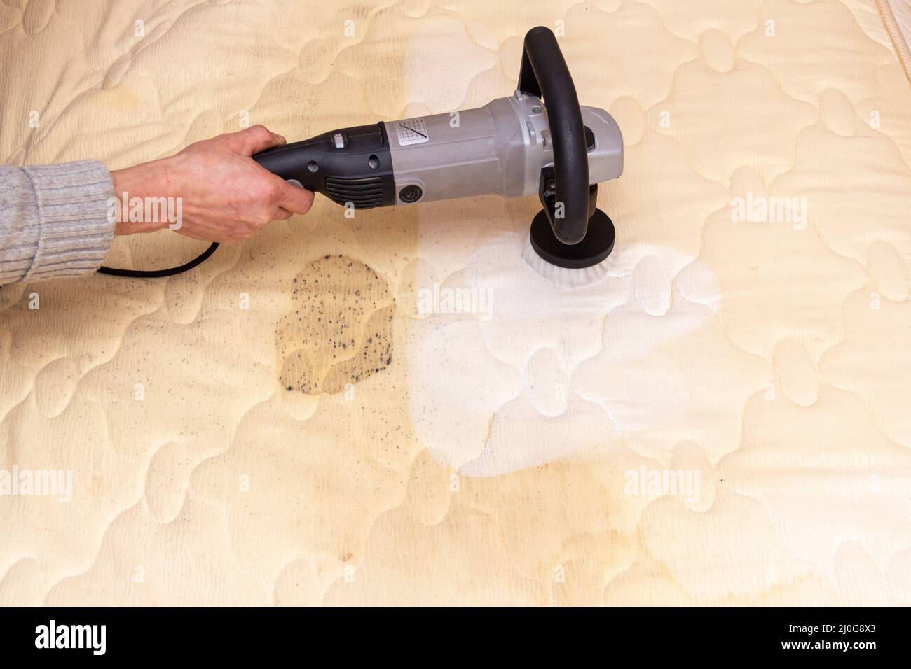 A man cleans a dirty mattress with an electric brush Stock Photo