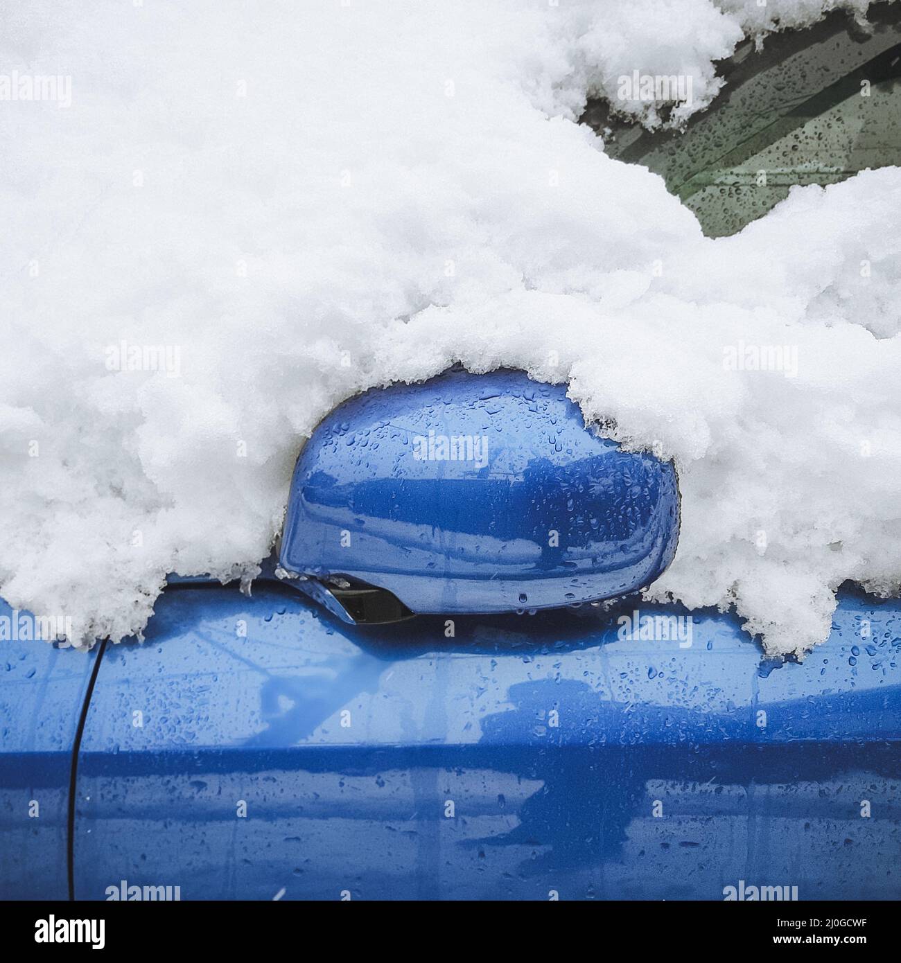 A fragment of a wet blue car covered with snow with a folded rear-view mirror. Closeup photo Stock Photo
