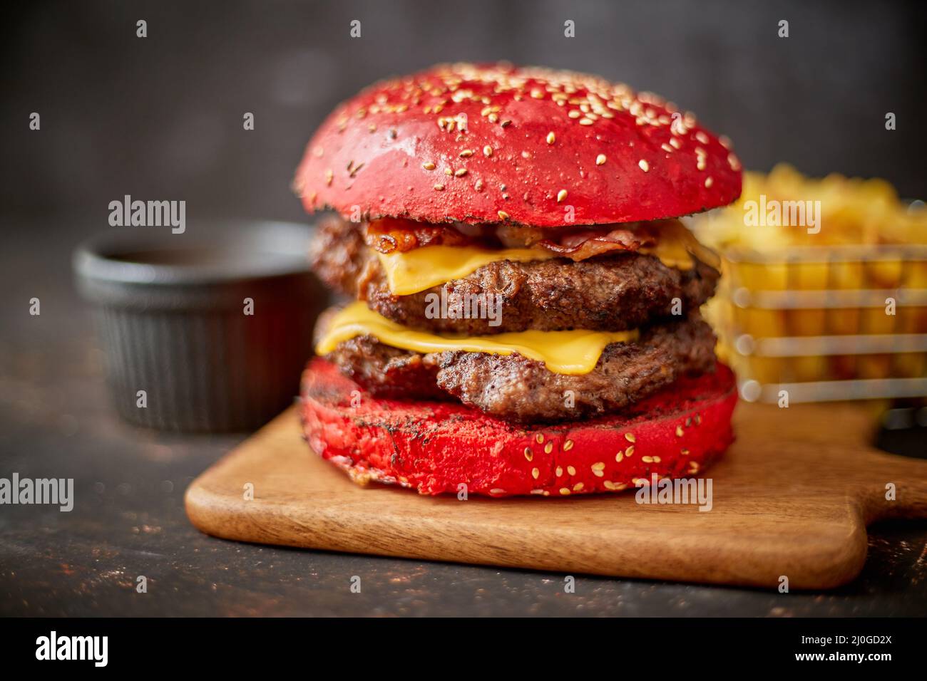 Homemade red sesame bun double bacon cheese burger. Served with french fries on wooden board. Stock Photo