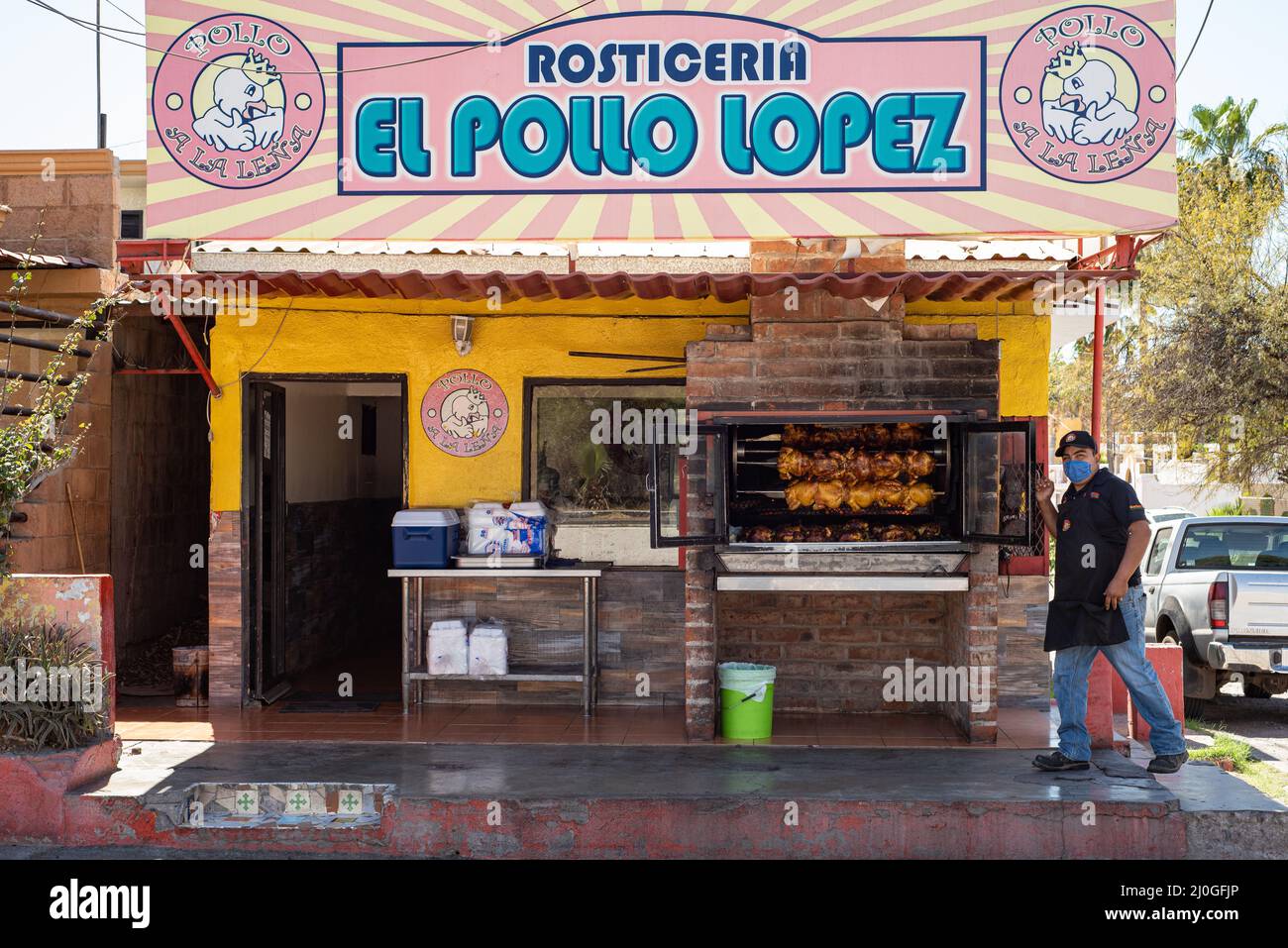 A cook stands next to chickens rotating on a spit in a storefront rotisserie oven for El Pollo Lopez in San Carlos, Sonora, Mexico. Stock Photo