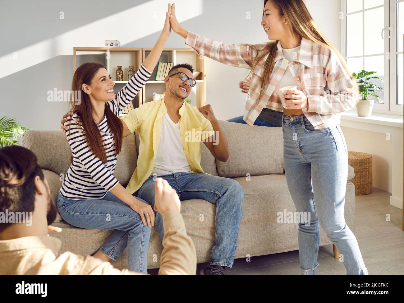 Happy excited young women give high fiving each other while having fun at home with friends. Stock Photo