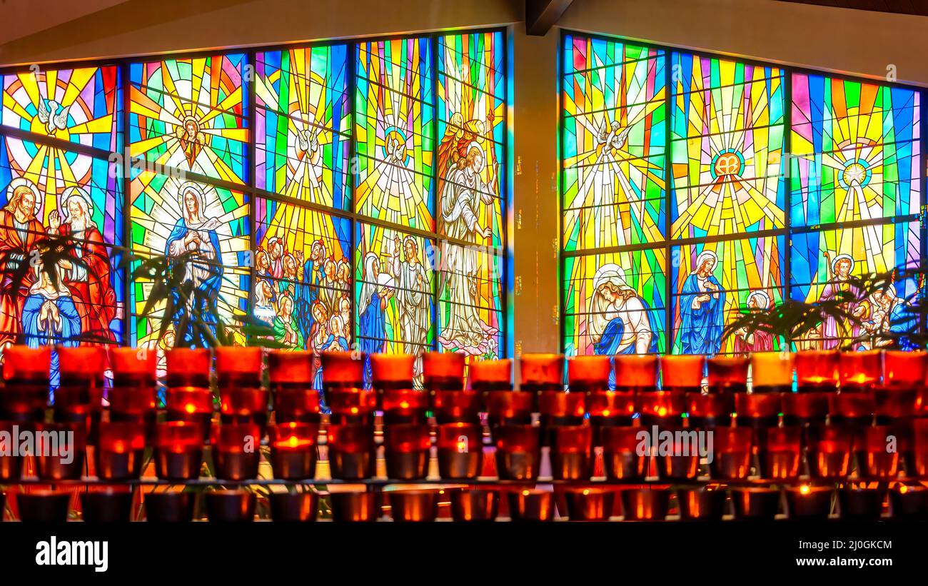 Light a candle altar with stained-glass window with Christian religious symbols seen in the Annunciation of the Blessed Virgin Mary Catholic Church Stock Photo