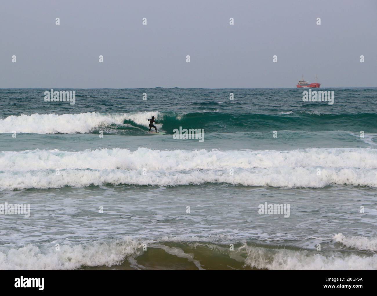 Lady Alexandra cargo ship manoeuvring to anchor off the beach with a surfer Sardinero Santander Cantabria Spain Stock Photo