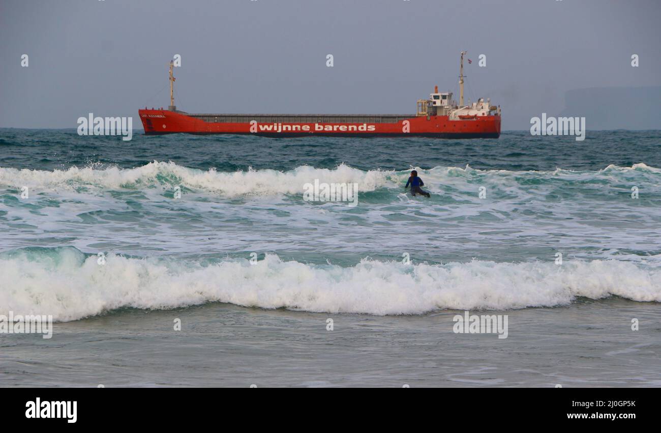 Lady Alexandra cargo ship manoeuvring to anchor off the beach with a surfer Sardinero Santander Cantabria Spain Stock Photo