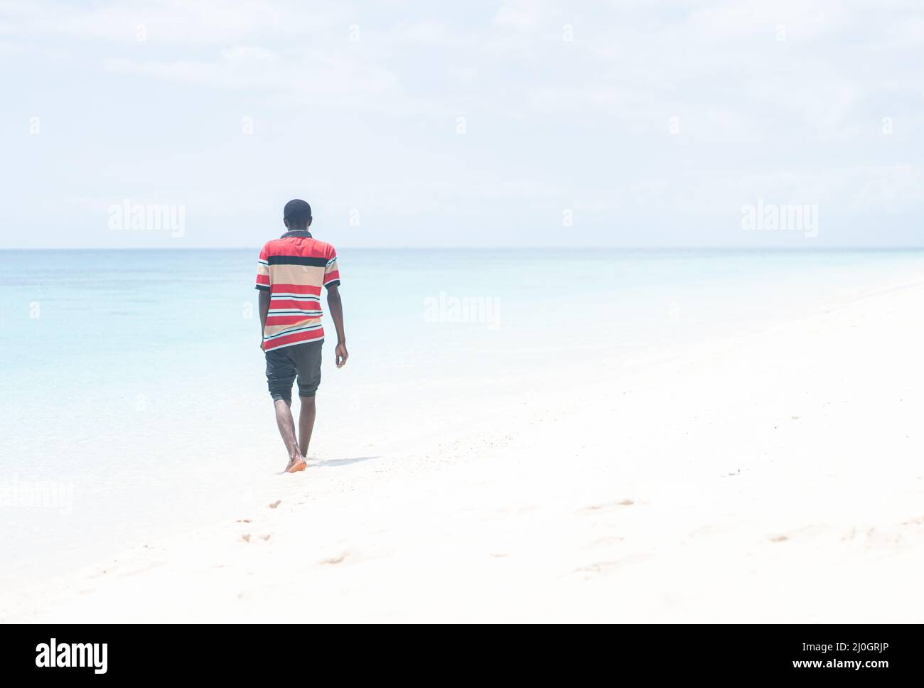 Black African young man walking on tropical beach Stock Photo