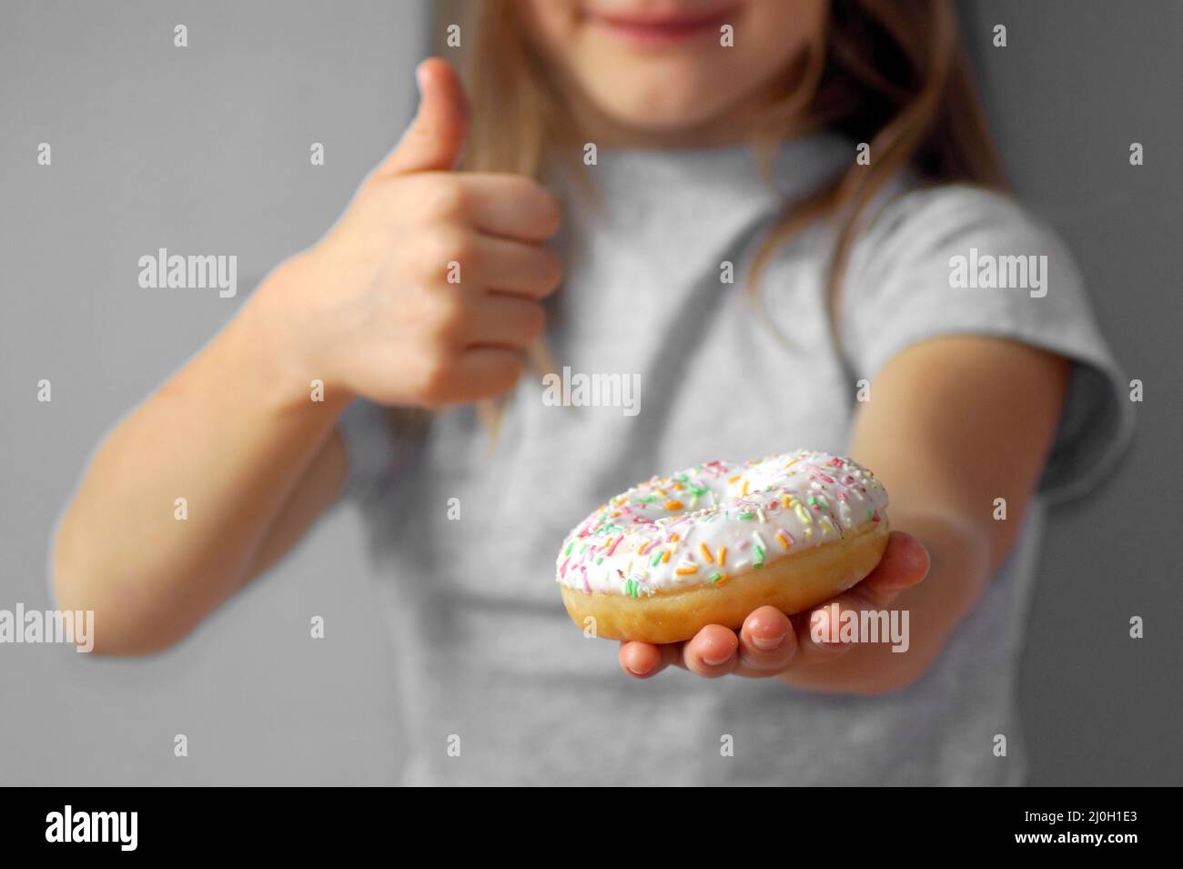 The child shows with a gesture - thumbs up - that the donut is very tasty and you need to buy it Stock Photo