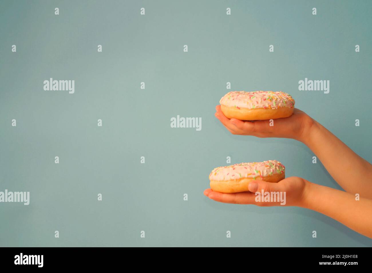 The child holds in his hands two donuts with multi-colored sprinkles, on a gray-blue background. Focus on the top donut. Hands are shifted to the edge Stock Photo