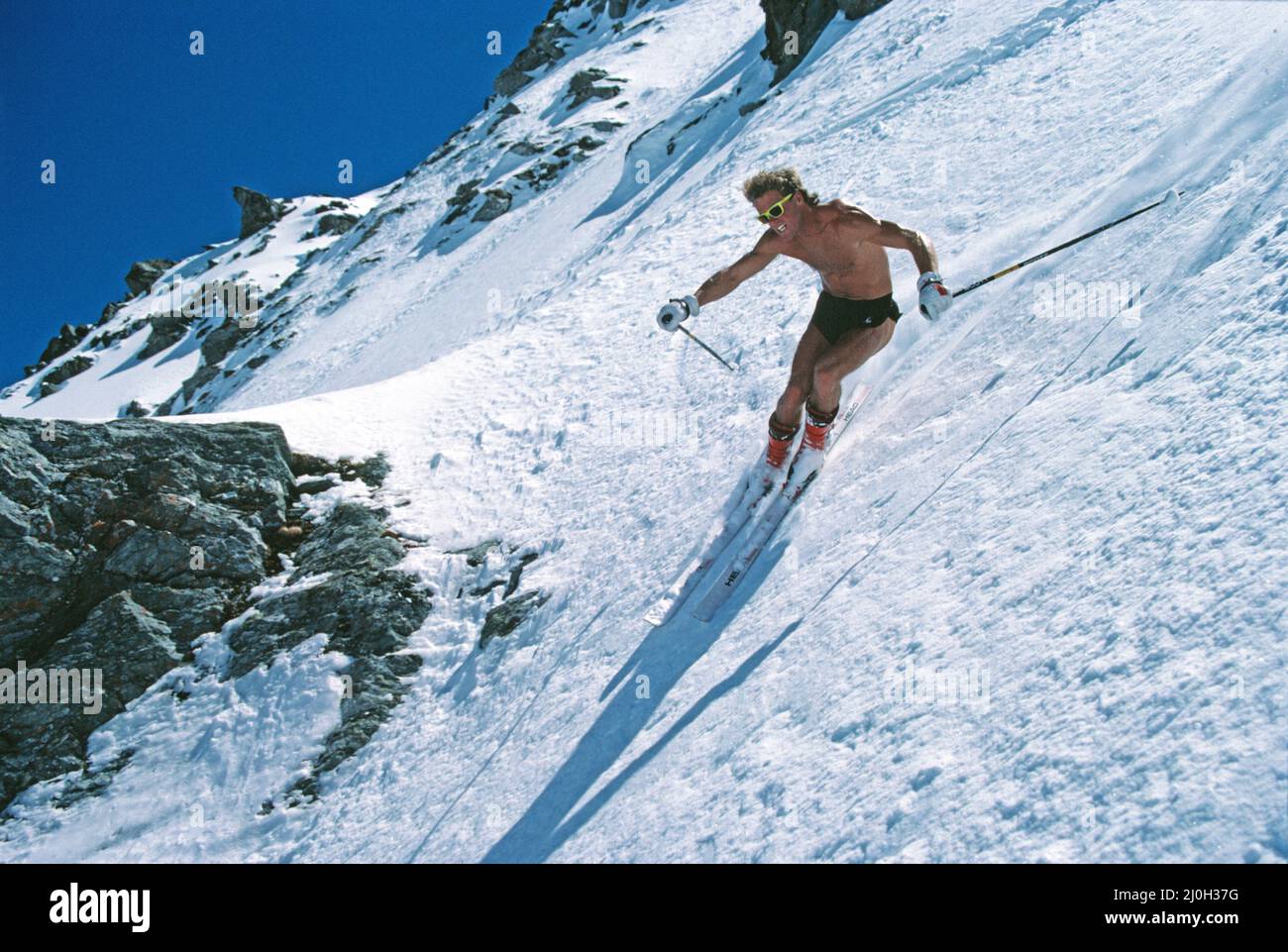 New Zealand. Snow skiing. Young man downhill skiing in shorts, bare-chested. Stock Photo