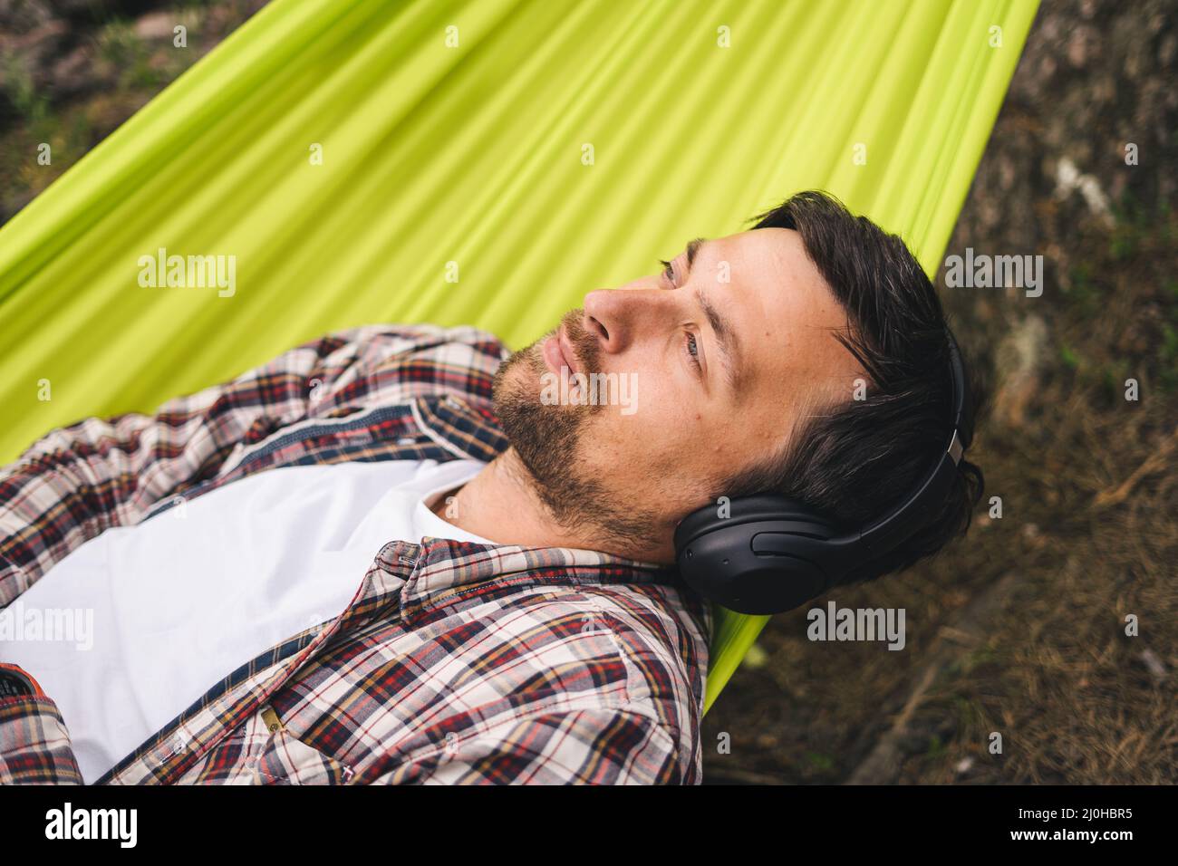 Young caucasian man resting in hammock, listening to music on headphones and using smartphone afterwards on bicycle in forest ne Stock Photo