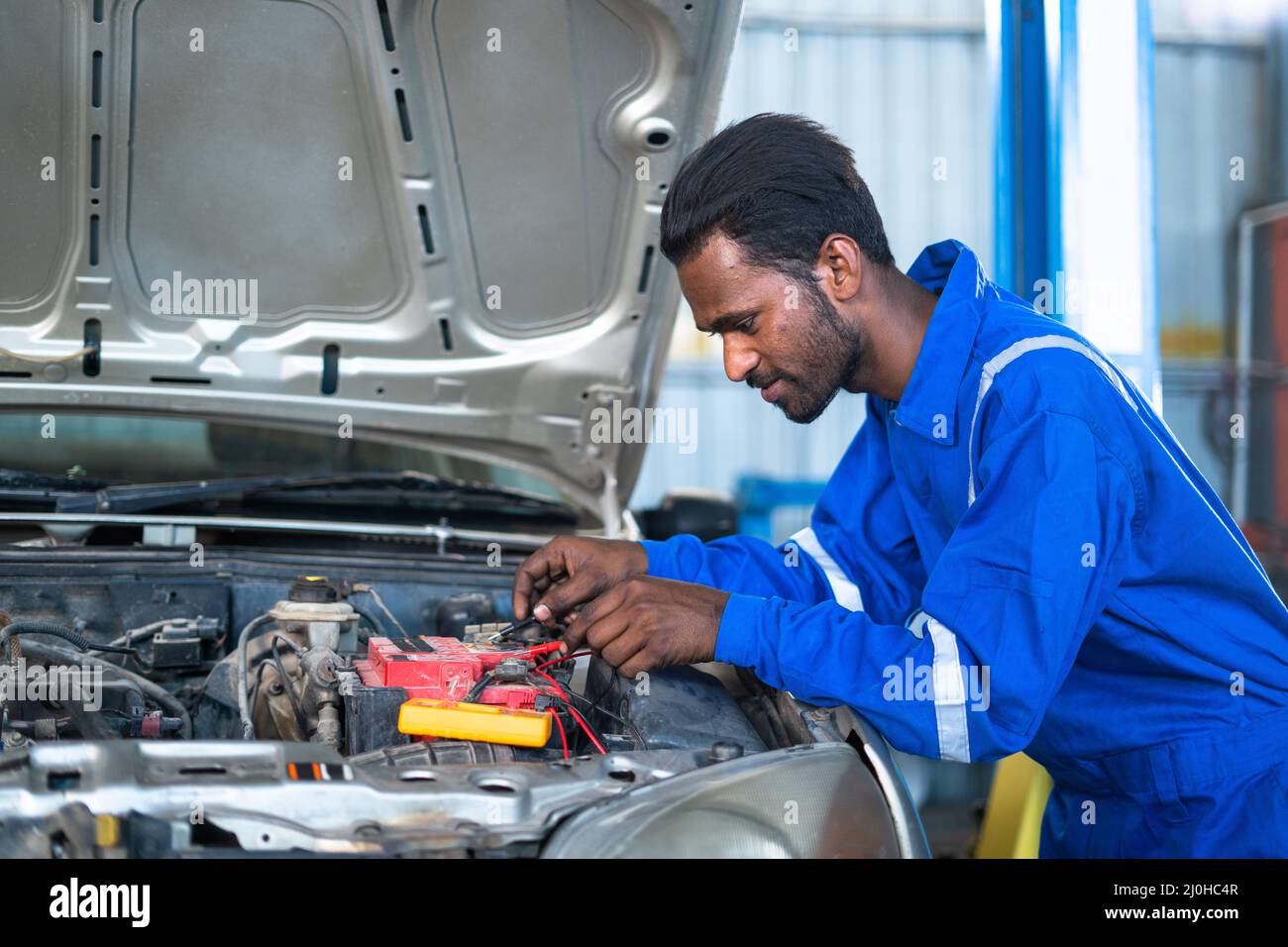 Car mechanic testing or checking car engine battery by using digital multimeter at garage - concept of technology, maintenance services and blue Stock Photo
