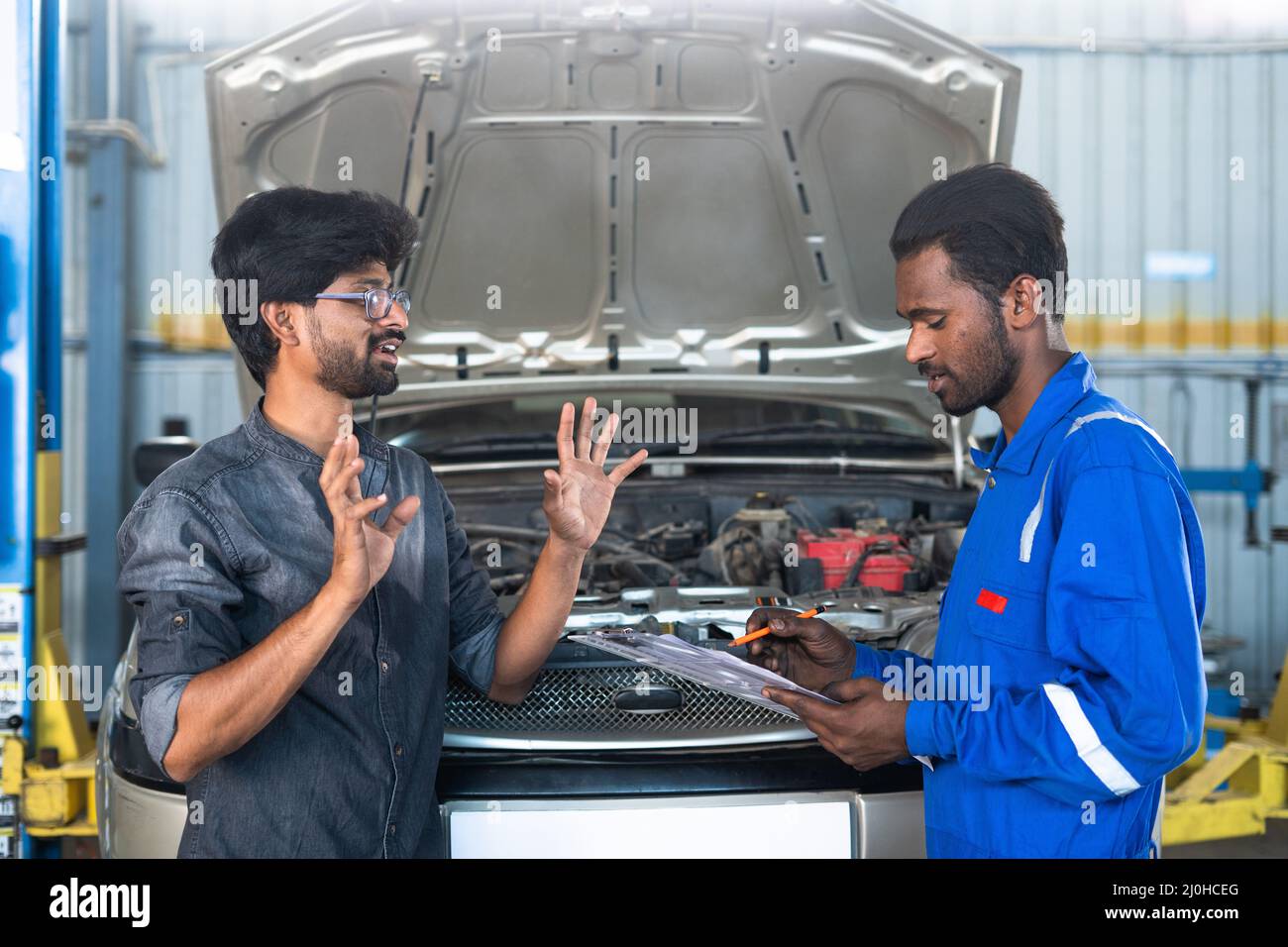 Customer explaining car engine problem while Mechanic noting problems at garage - concept of customer communication, car maintenance service and Stock Photo