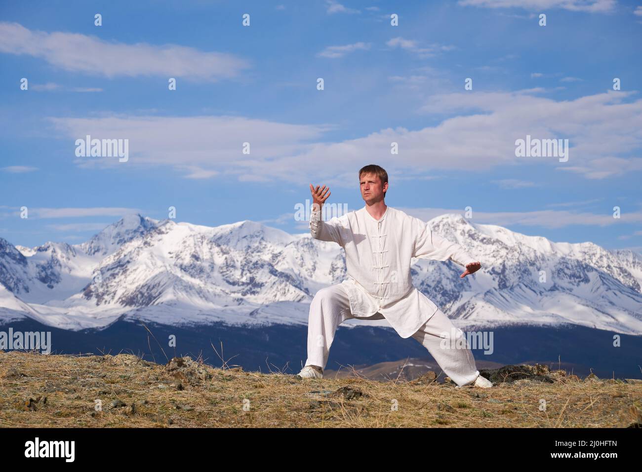 Wushu master in a white sports uniform training kungfu in nature on background of snowy mountains. Stock Photo