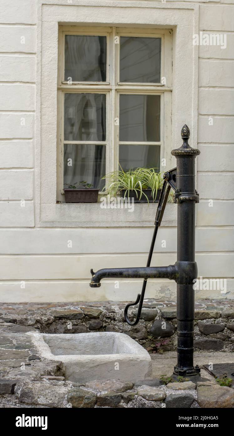 Old antique hand operated water pump in front of the wall. Stock Photo