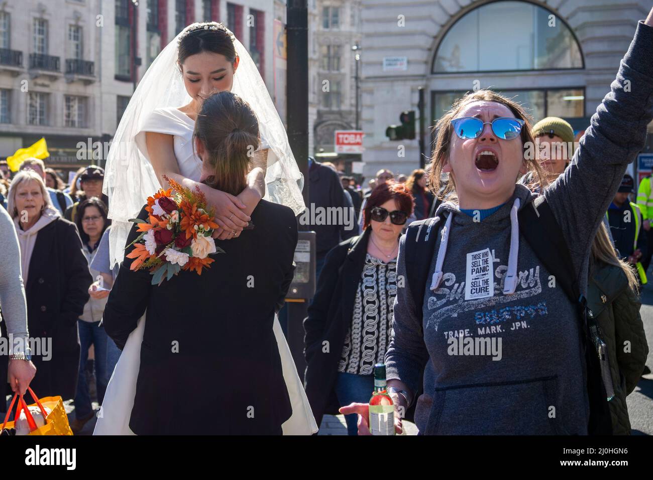 Westminster, London, UK. 19th Mar, 2022.A protest is taking place against vaccinating children for Covid 19, joined by anti-vaxxers. The march interrupted a wedding dress photoshoot with the Asian bride and white groom continuing regardless. Female chanting Stock Photo