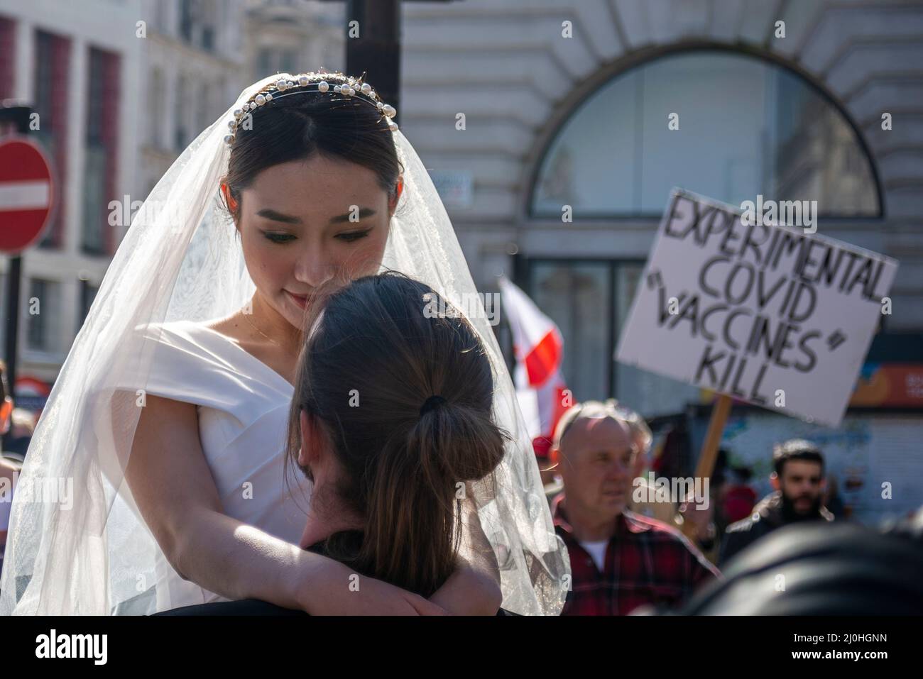 Westminster, London, UK. 19th Mar, 2022.A protest is taking place against vaccinating children for Covid 19, joined by anti-vaxxers. The march interrupted a wedding dress photoshoot with the Asian bride and white groom continuing regardless. Covid placard Stock Photo