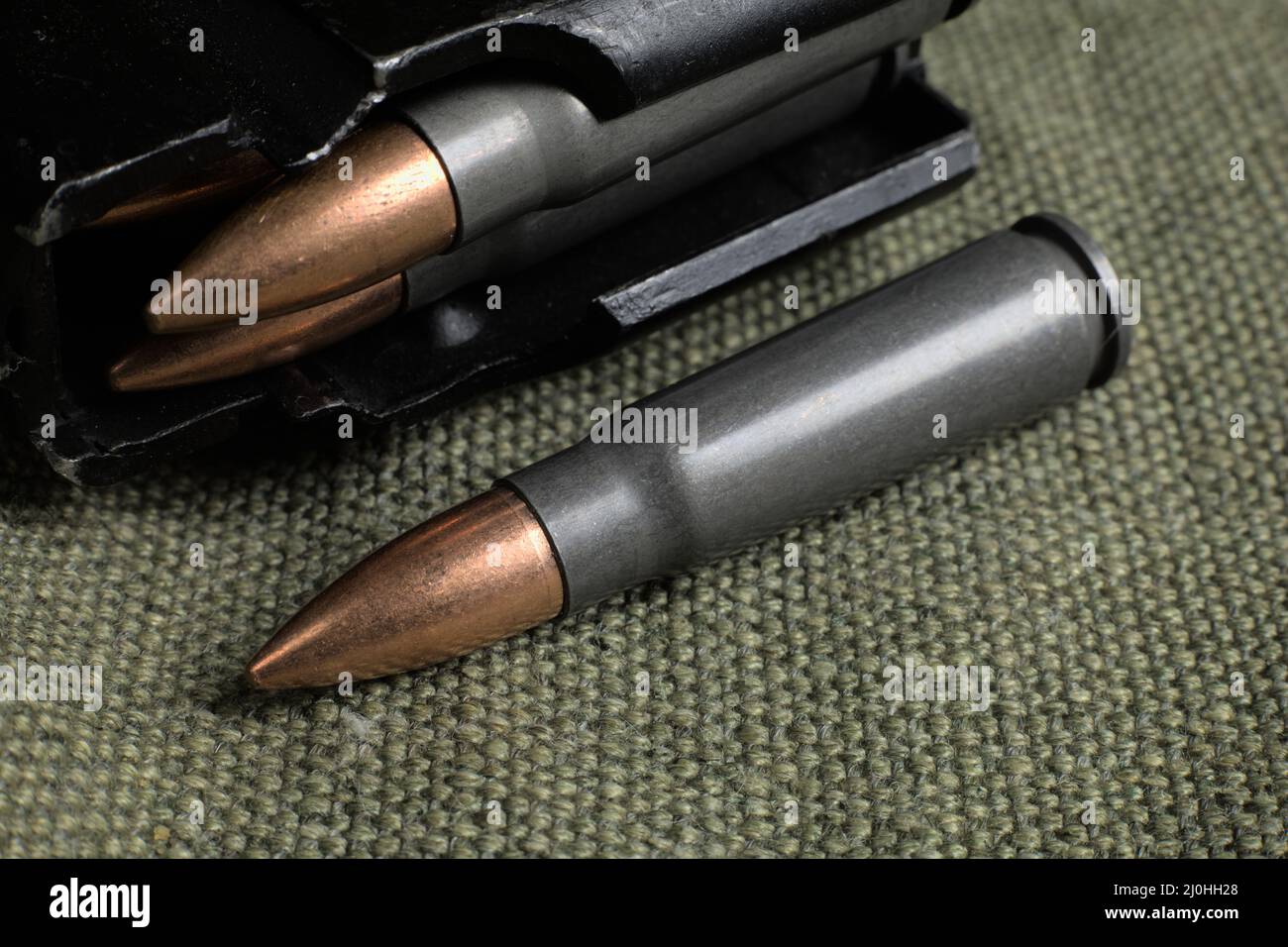 loaded magazine of Ak-47 and a single cartridge (7,62x39mm) lying on a military canvas background Stock Photo