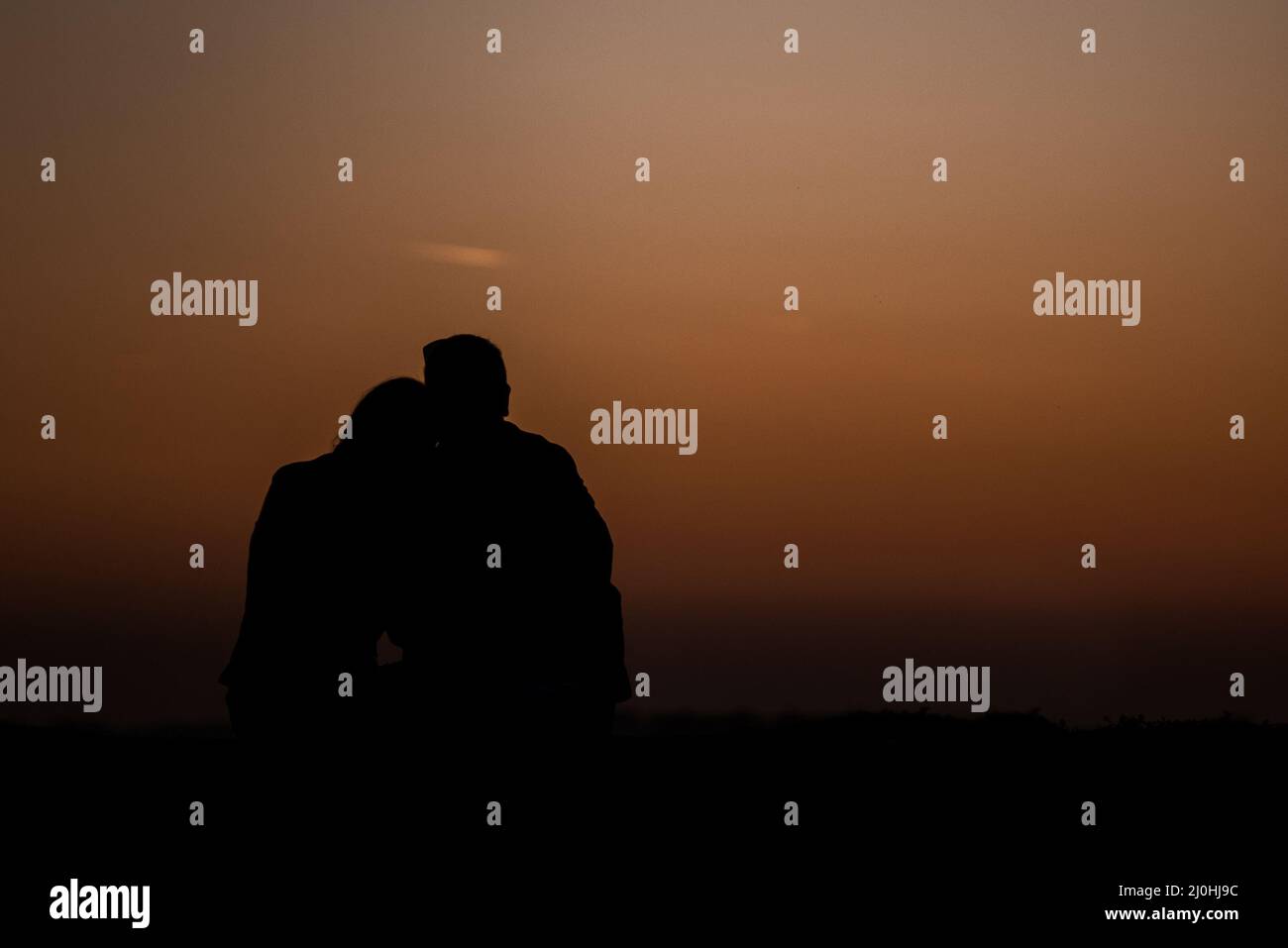 Silhouettes of a man and a woman hugging against a colorful evening sky ...