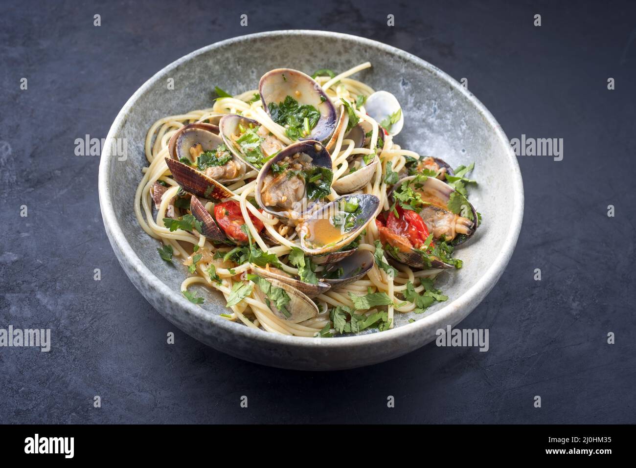 Spaghetti alle vongole with tomato in seafood jus served as close-up at a Nordic design bowl with copy space Stock Photo