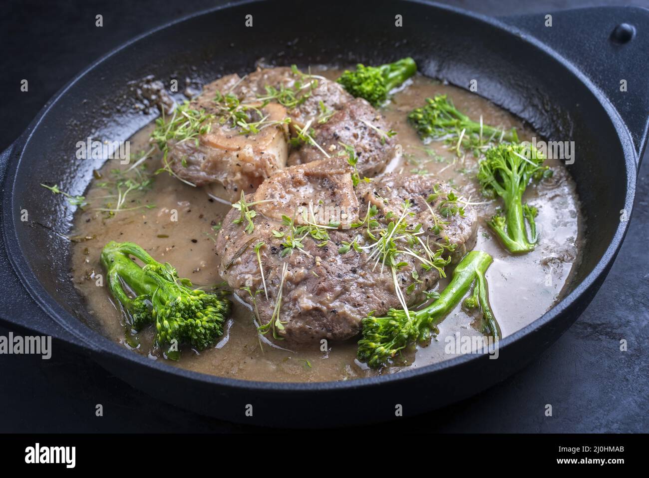 Modern style traditional braised Italian ossobuco alla Milanese with baby broccoli and herb in white wine meat sauce served in a Stock Photo