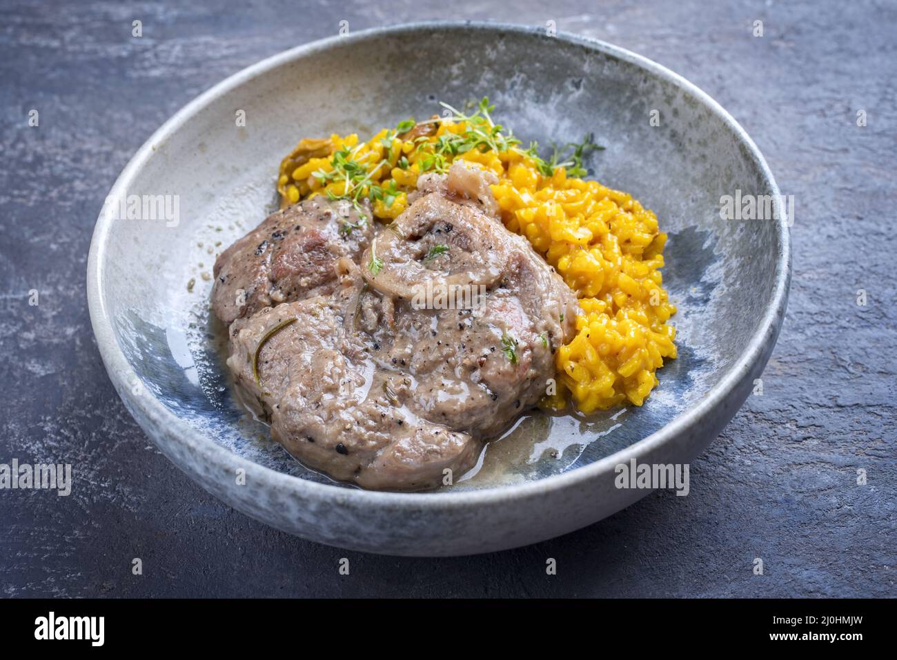 Modern style traditional braised Italian ossobuco alla Milanese with saffron risotto and herbs in white wine meat sauce served a Stock Photo
