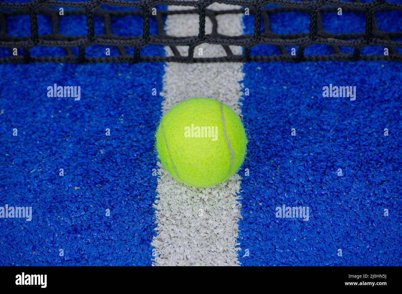 Paddle tennis ball on the service line and near the net of a blue