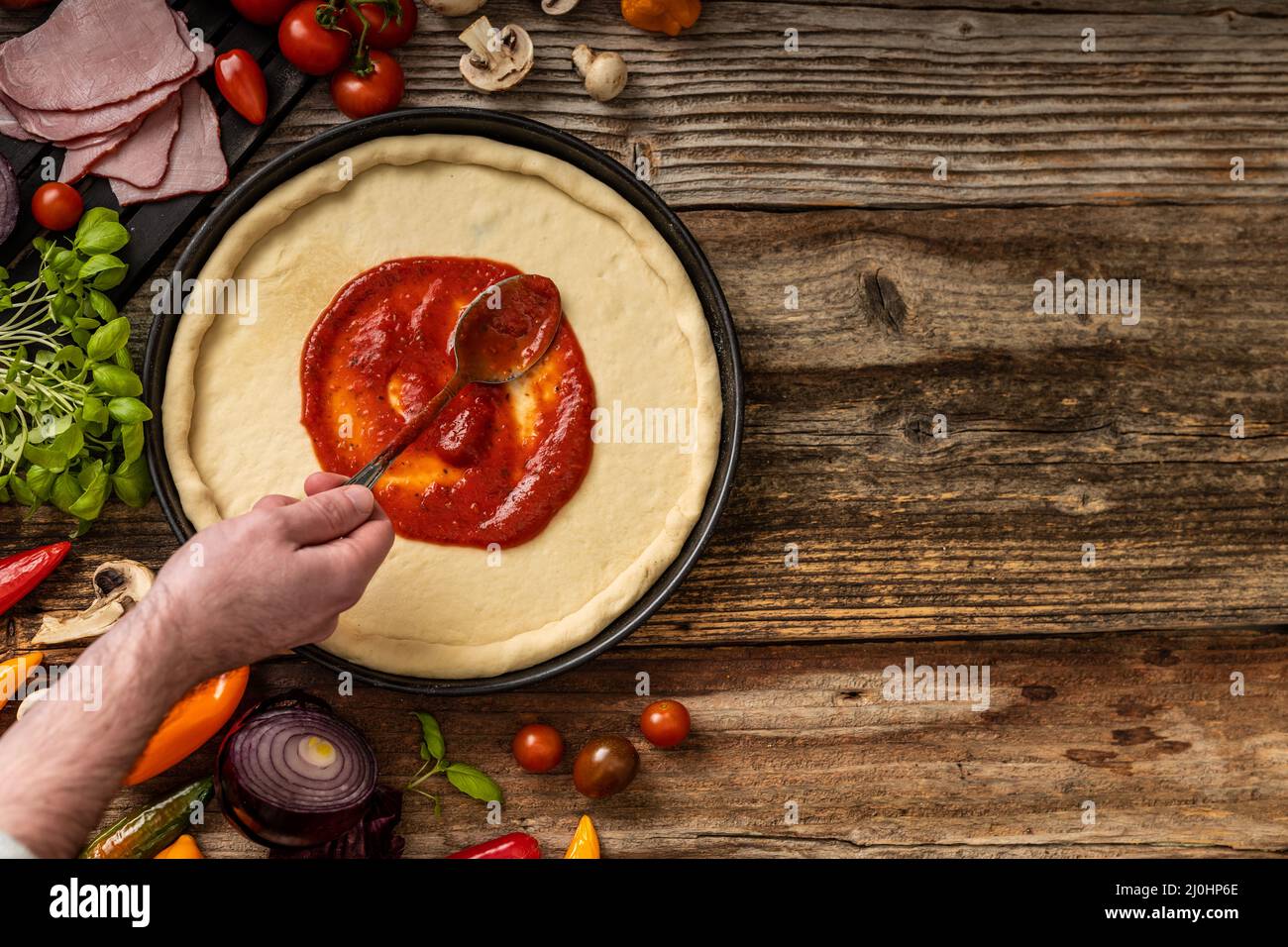 Raw delicious pizza dough with red souce on the wooden table Stock Photo
