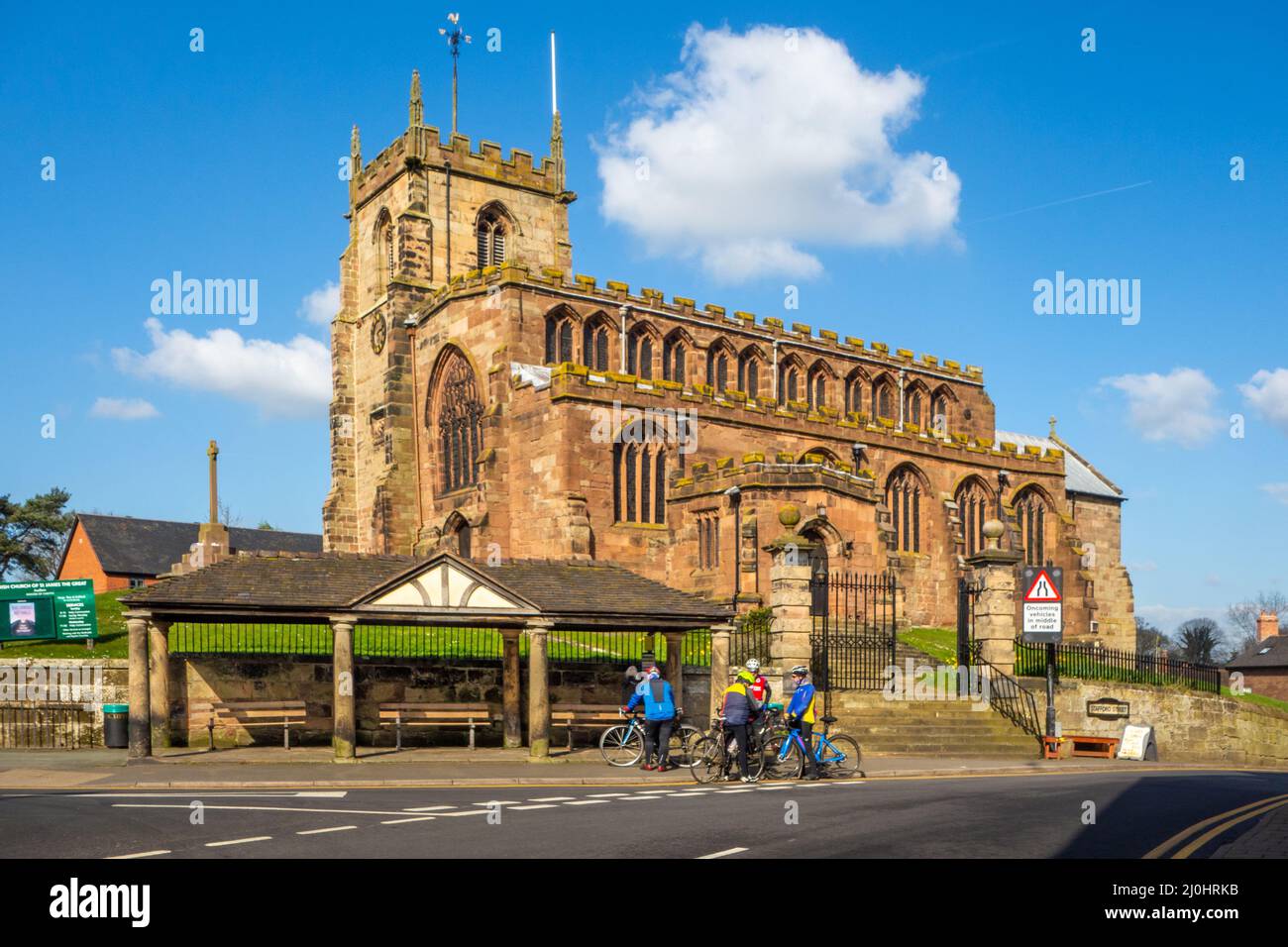 Cyclists stopped for a rest outside the parish church of  St James the Great in the Cheshire village of Audlem, Stock Photo