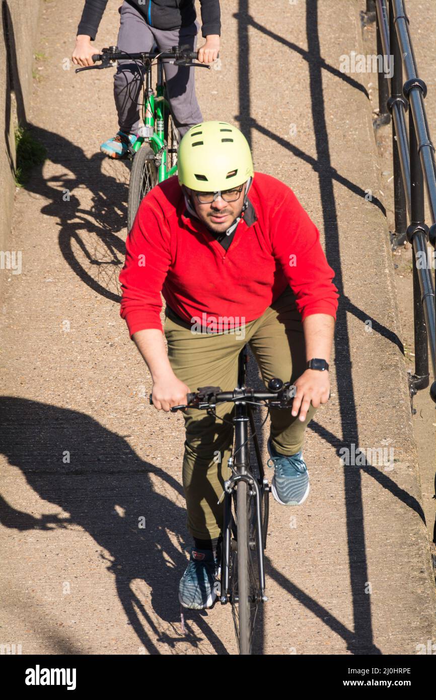A cyclist wearing a yellow helmet and red jumper cycling in bright sunlight Stock Photo