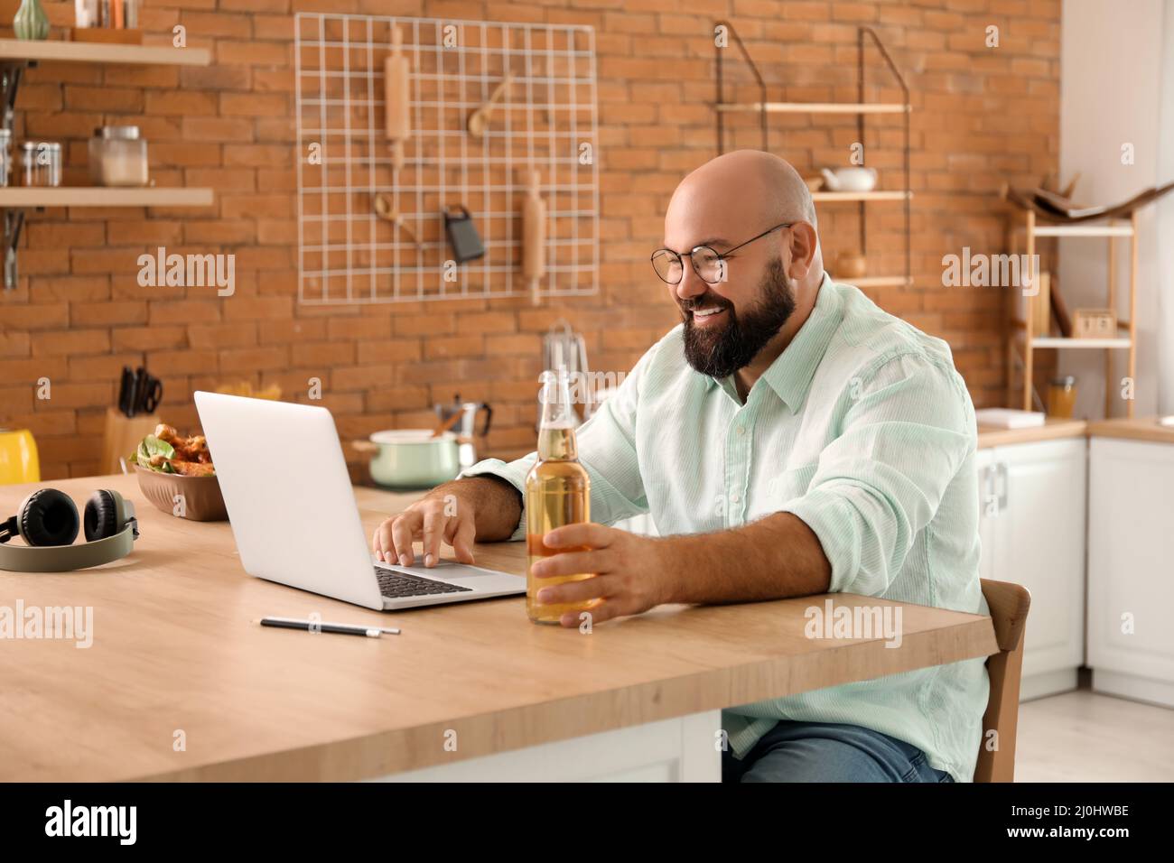 Bald man with laptop drinking beer in kitchen Stock Photo - Alamy