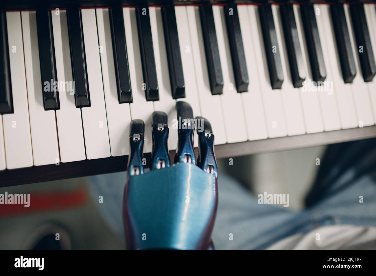 Young disabled man play on piano electronic synthesizer with artificial prosthetic hand in music shop. Stock Photo