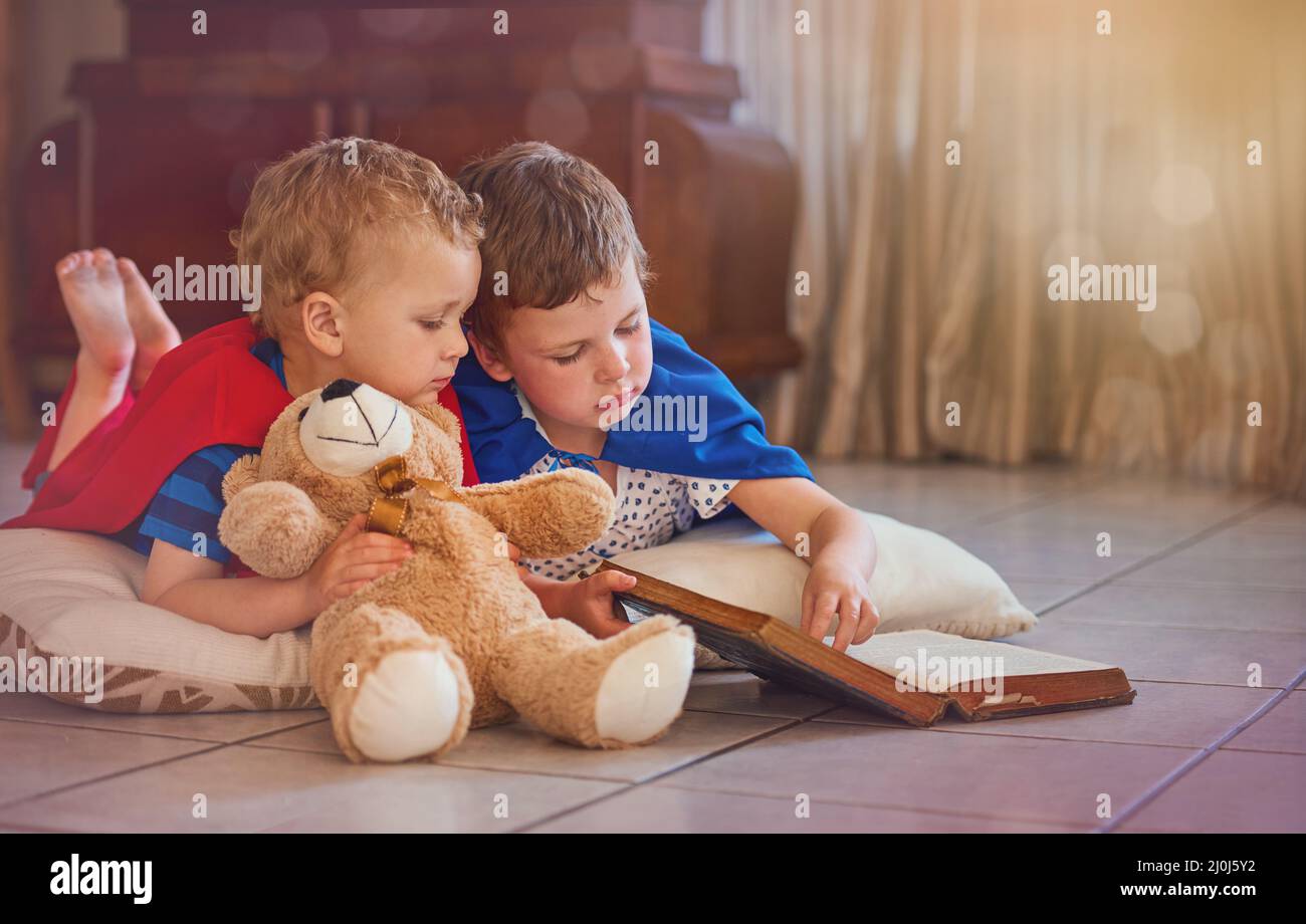 Says right here you should do what I tell you. Shot of two little boys playing with a book while lying on the floor at home. Stock Photo