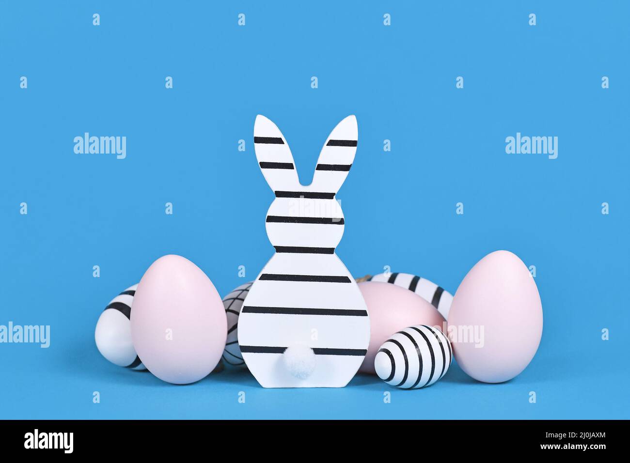 Striped black and white and pink easter bunny ornament and eggs on blue background Stock Photo