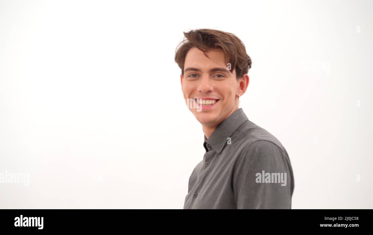 Smiling handsome young man turn fixing his hair and looking at camera wearing grey shirt isolated on white background. 4K video Stock Photo