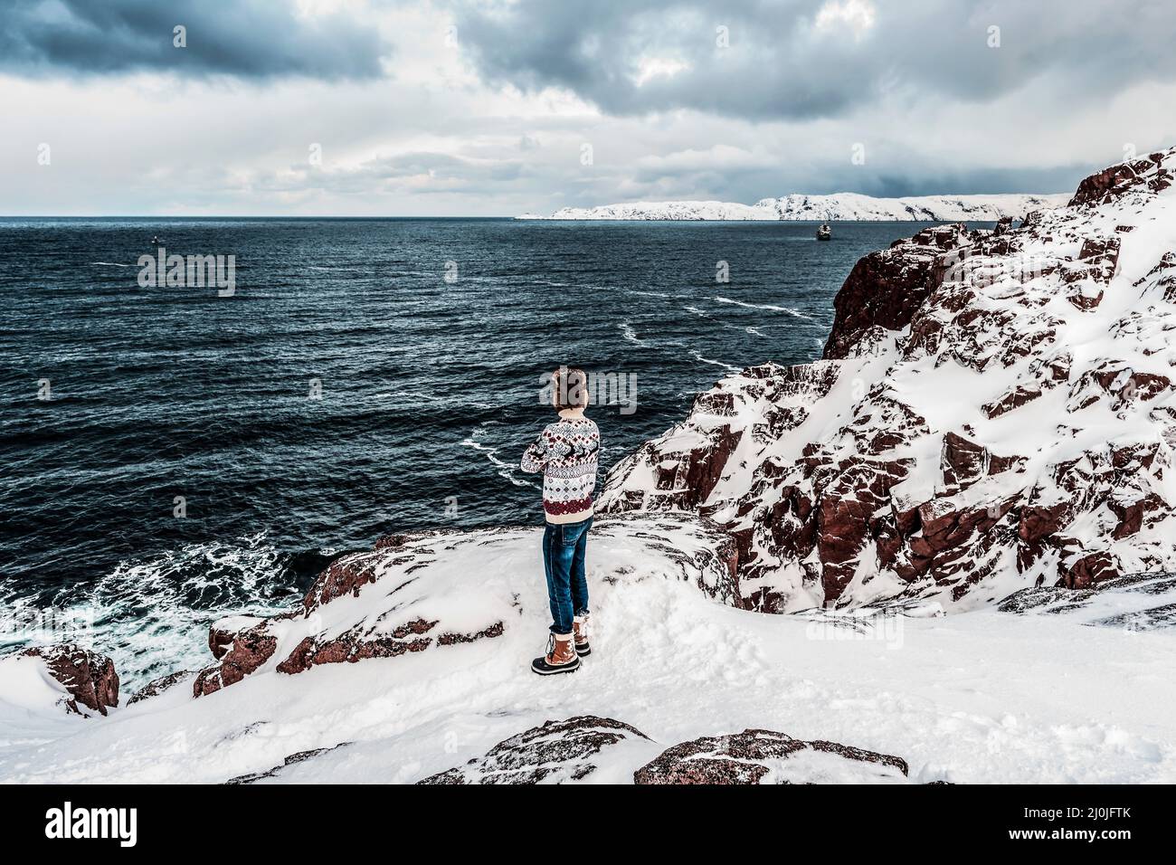 A man standing on a mountain and looking at the sea with dramatic clouds Stock Photo