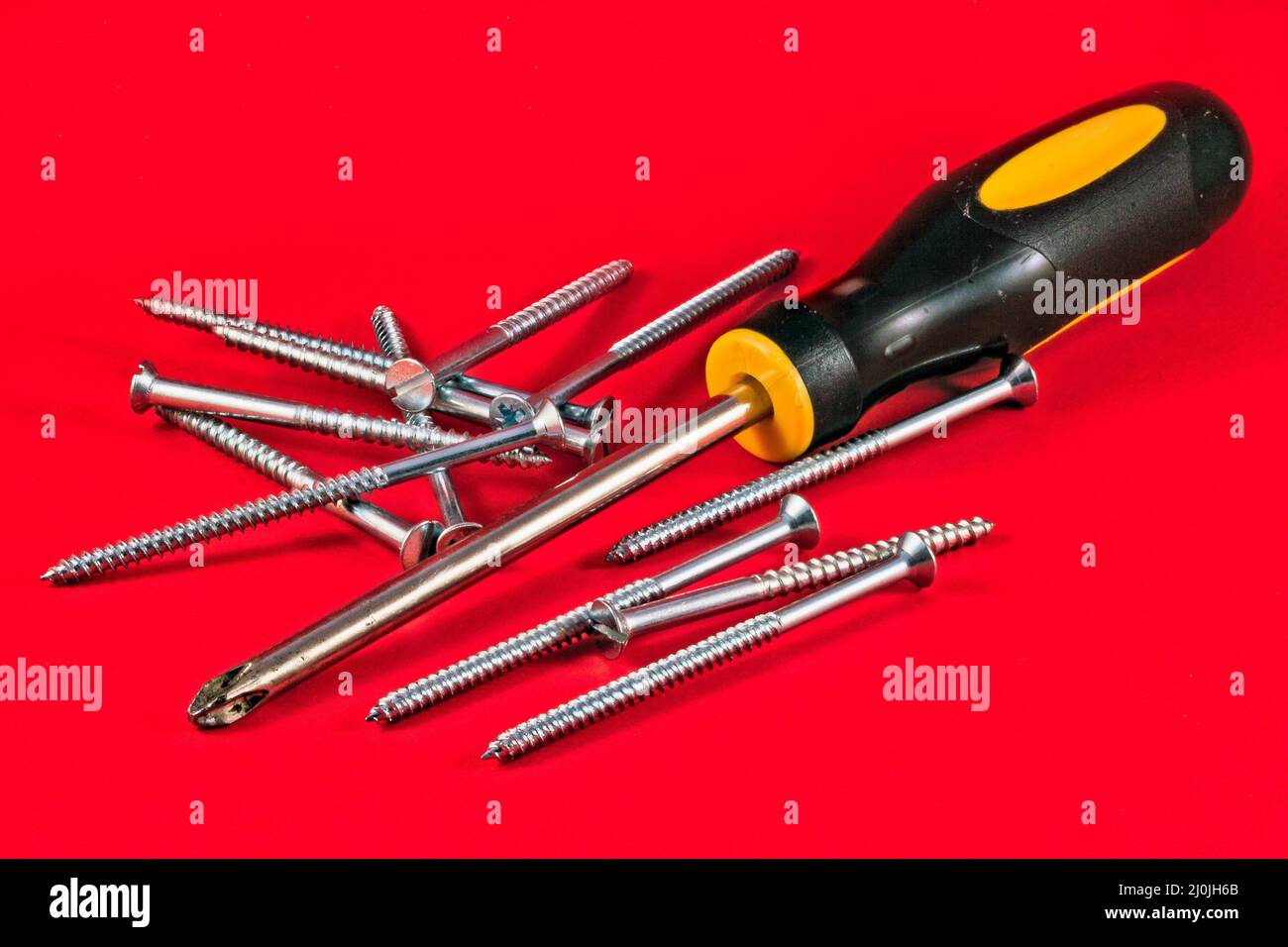 Screw driver and screws against a red background Stock Photo