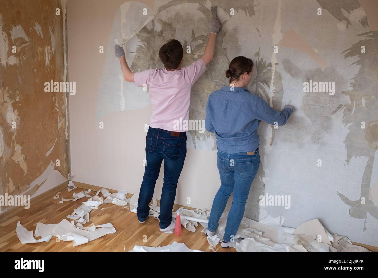 Young caucasian couple removing old wallpaper from walls preparing for