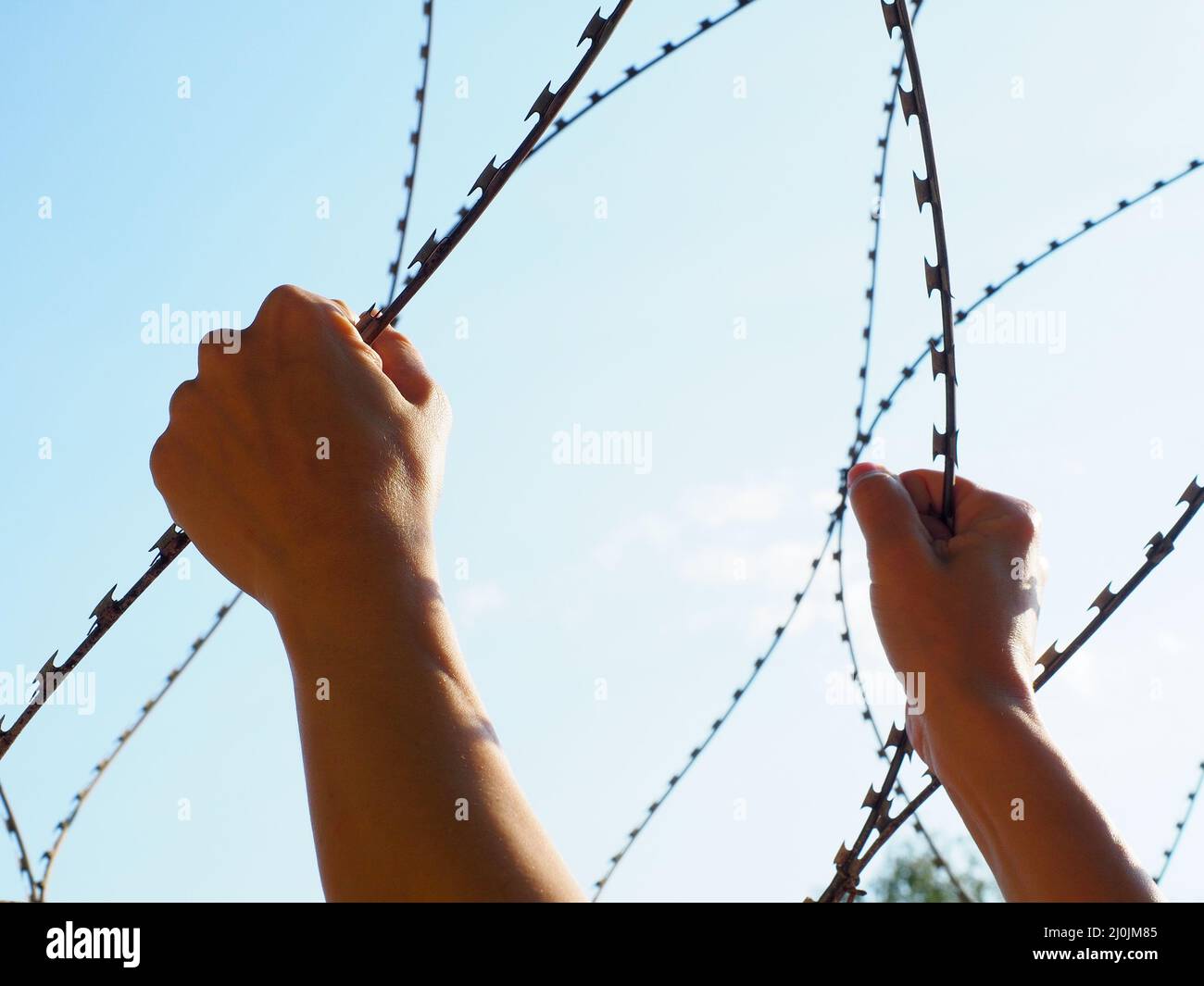 Two hands holding a barbed wire against the blue sky Stock Photo