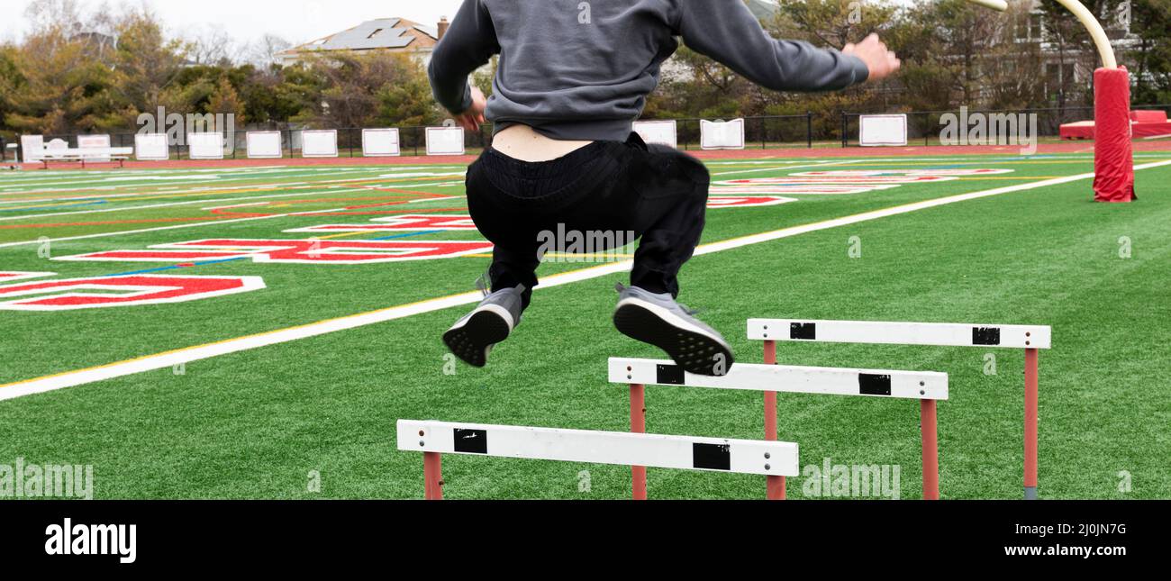A high school track and field runner is jumping over track hurdles