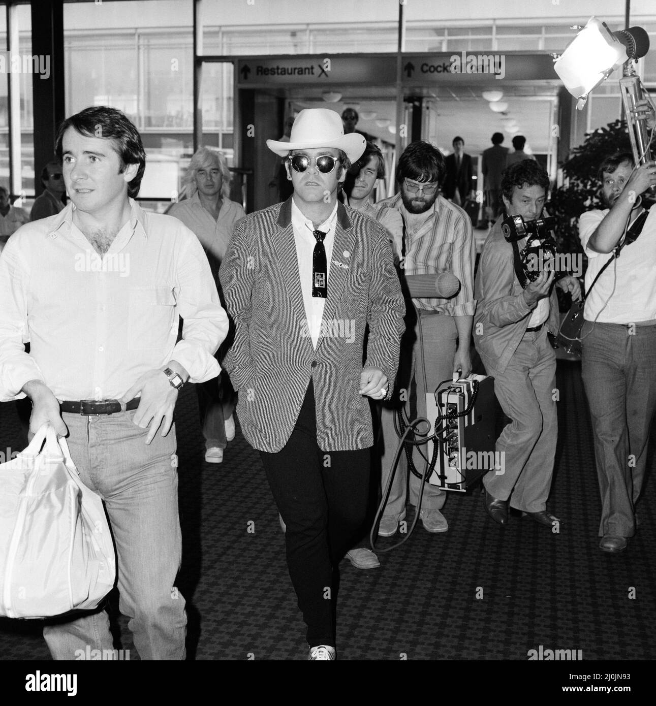 Dressed in a stetson hat, Elton John leaves Heathrow Airport for America. On the left is John Reid, Elton's manager. 10th August 1980. Stock Photo