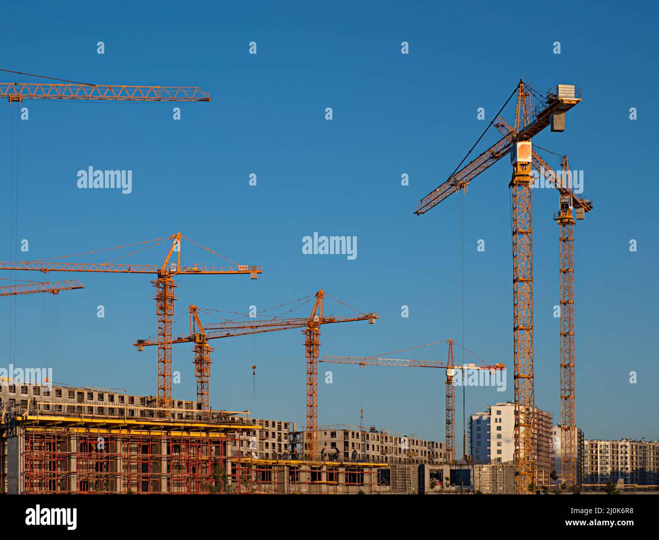 Some tower cranes on background of blue sky and Industrial workers and builders with hardhat in uniform pour concrete at construction site Stock Photo