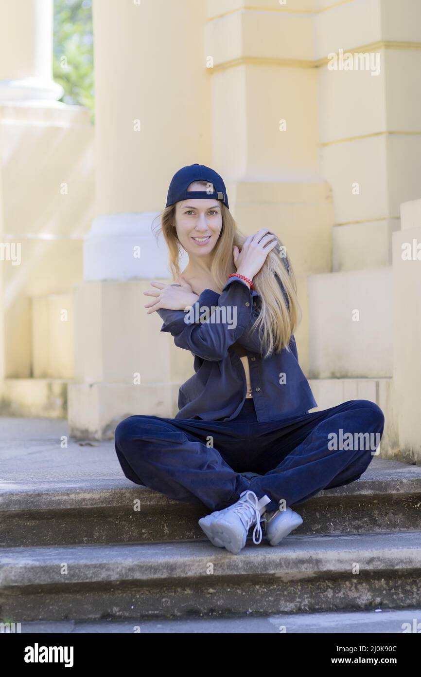 Smiling long-haired blonde woman in sportswear sits on steps in park architecture Stock Photo