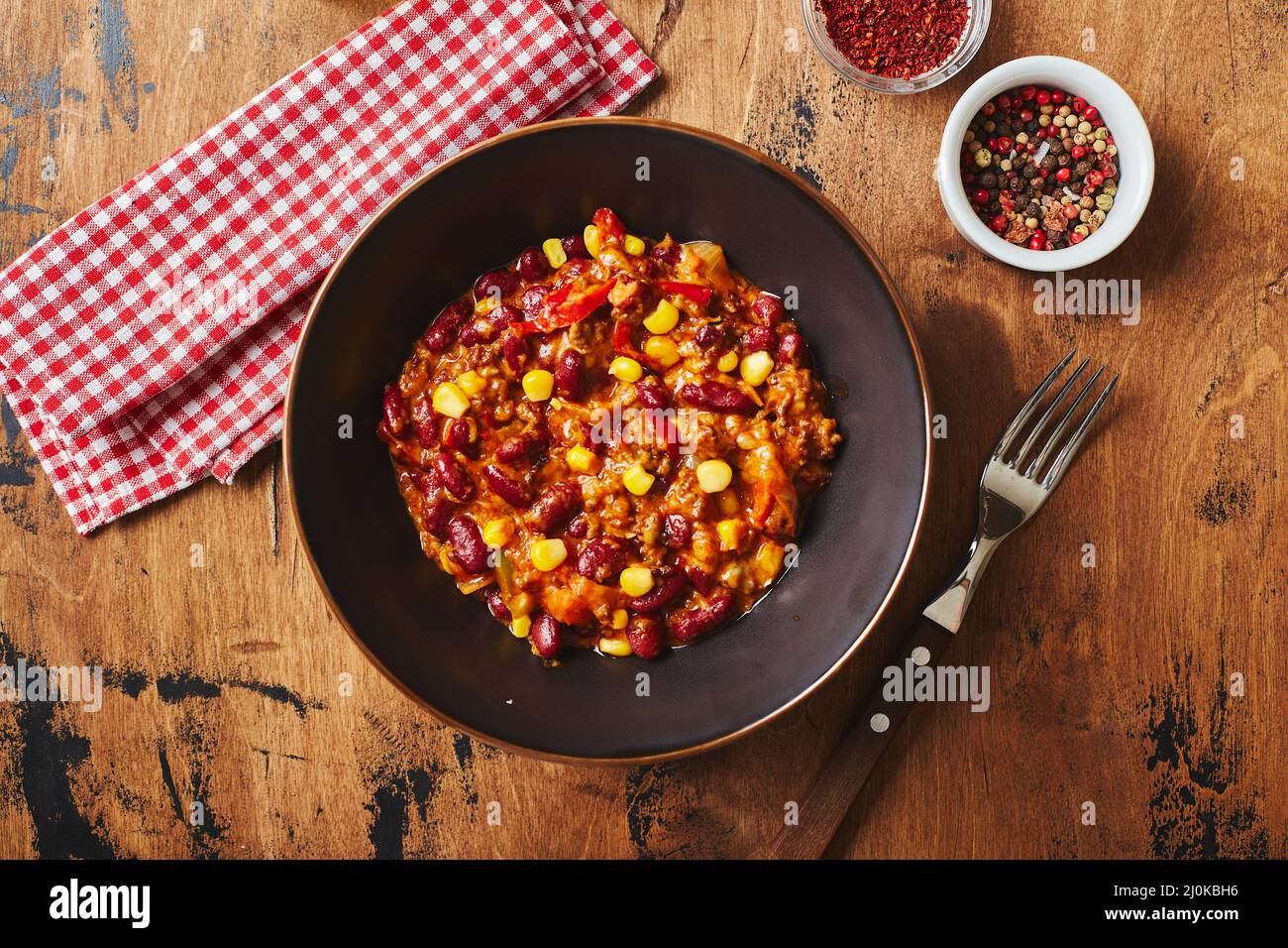 Chili Con Carne with ground beef, beans and corn in dark bowl on wooden ...