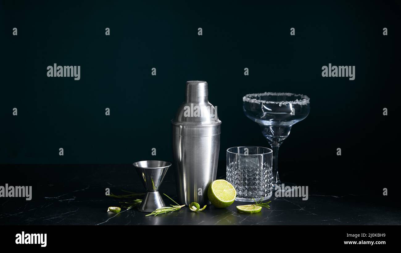 Cocktail shaker and cocktail glasses, and ingredients on dark marble